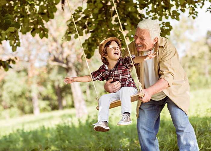 Image of elderly man playing with his grandson on a swing.